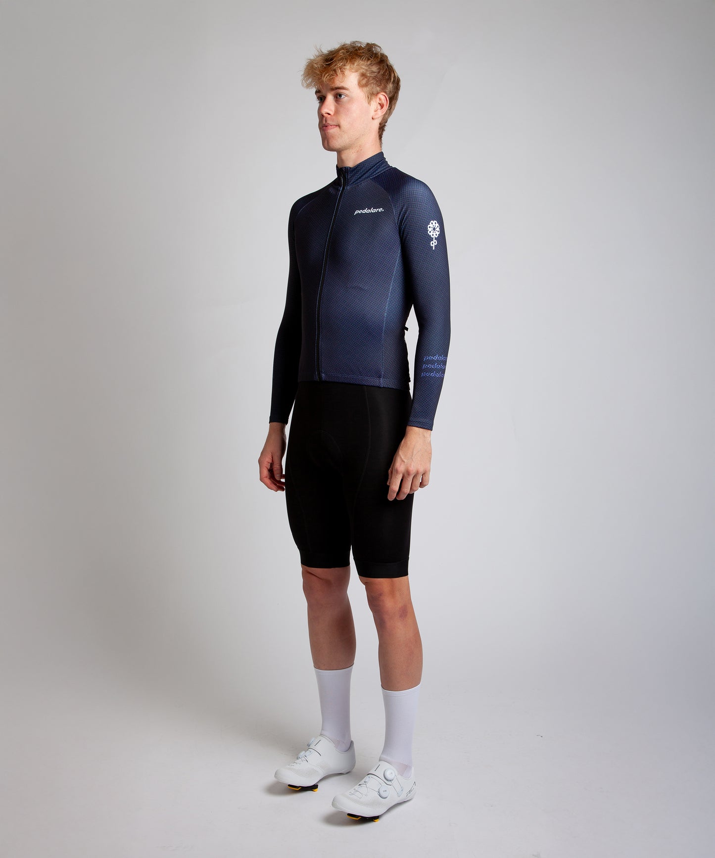Male cyclist modelling Pedalare’s navy winter long sleeve cycling jersey, paired with black bib shorts. Side profile studio shot highlighting the jersey’s thermal fabric, streamlined fit, and subtle branding. Designed by Perth cycling brand Pedalare for cool-weather performance and style. Men’s winter cycling jersey ideal for road cyclists seeking aero cycling gear and premium cycling apparel.