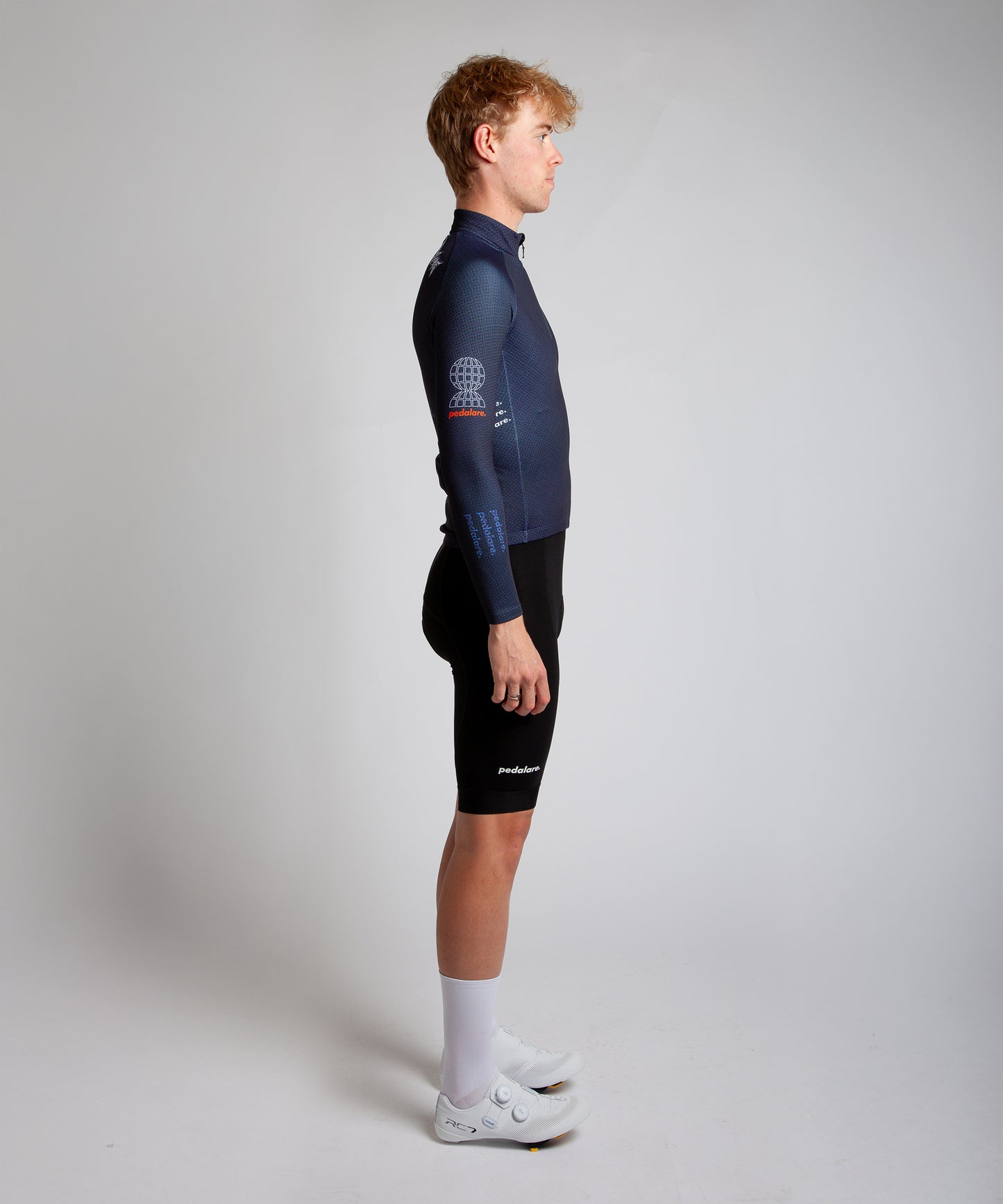 Male cyclist modelling Pedalare’s navy winter long sleeve cycling jersey, paired with black bib shorts. Side profile studio shot highlighting the jersey’s thermal fabric, streamlined fit, and subtle branding. Designed by Perth cycling brand Pedalare for cool-weather performance and style. Men’s winter cycling jersey ideal for road cyclists seeking aero cycling gear and premium cycling apparel.
