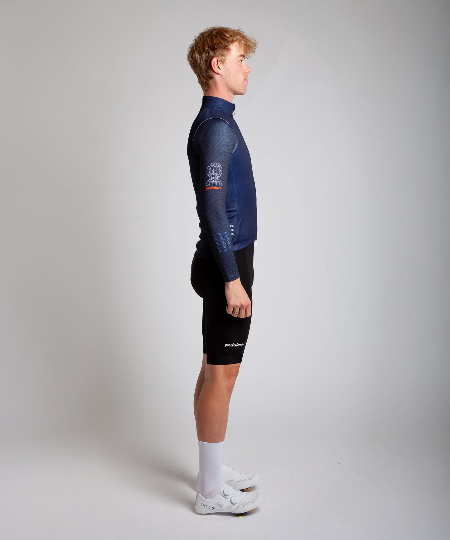 Male men’s cyclist wearing Pedalare’s high-performance navy, blue cycling vest, layered over a navy long sleeve jersey and black bib shorts. Side profile studio shot showcasing the vest’s aerodynamic fit and premium detailing. Lightweight, windproof men’s cycling vest ideal for cool weather rides. Designed by Perth cycling brand Pedalare for performance, comfort, and style. Aero cycling gear for dedicated road cyclists.
