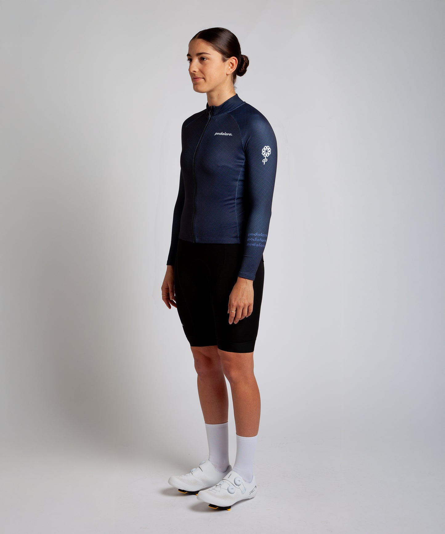 Female cyclist wearing Pedalare’s high-performance navy, blue cycling vest, layered over a navy long sleeve jersey and black bib shorts. Side profile studio shot showcasing the vest’s aerodynamic fit and premium detailing. Lightweight, windproof men’s cycling vest ideal for cool weather rides. Designed by Perth cycling brand Pedalare for performance, comfort, and style. Aero cycling gear for dedicated road cyclists.