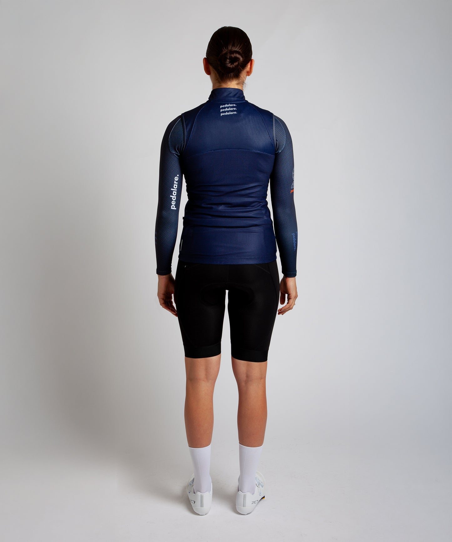 Female cyclist wearing Pedalare’s high-performance navy, blue cycling vest, layered over a navy long sleeve jersey and black bib shorts. Side profile studio shot showcasing the vest’s aerodynamic fit and premium detailing. Lightweight, windproof men’s cycling vest ideal for cool weather rides. Designed by Perth cycling brand Pedalare for performance, comfort, and style. Aero cycling gear for dedicated road cyclists.