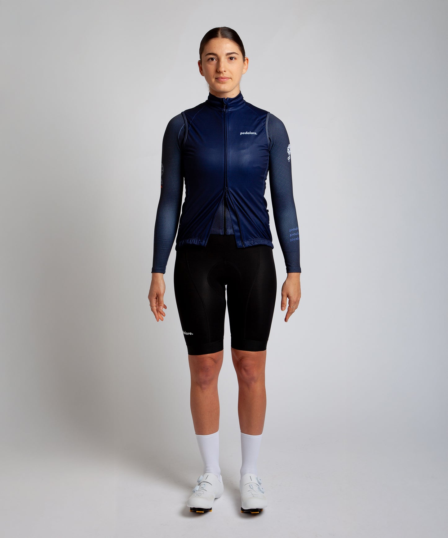 Female cyclist wearing Pedalare’s high-performance navy, blue cycling vest, layered over a navy long sleeve jersey and black bib shorts. Side profile studio shot showcasing the vest’s aerodynamic fit and premium detailing. Lightweight, windproof men’s cycling vest ideal for cool weather rides. Designed by Perth cycling brand Pedalare for performance, comfort, and style. Aero cycling gear for dedicated road cyclists.