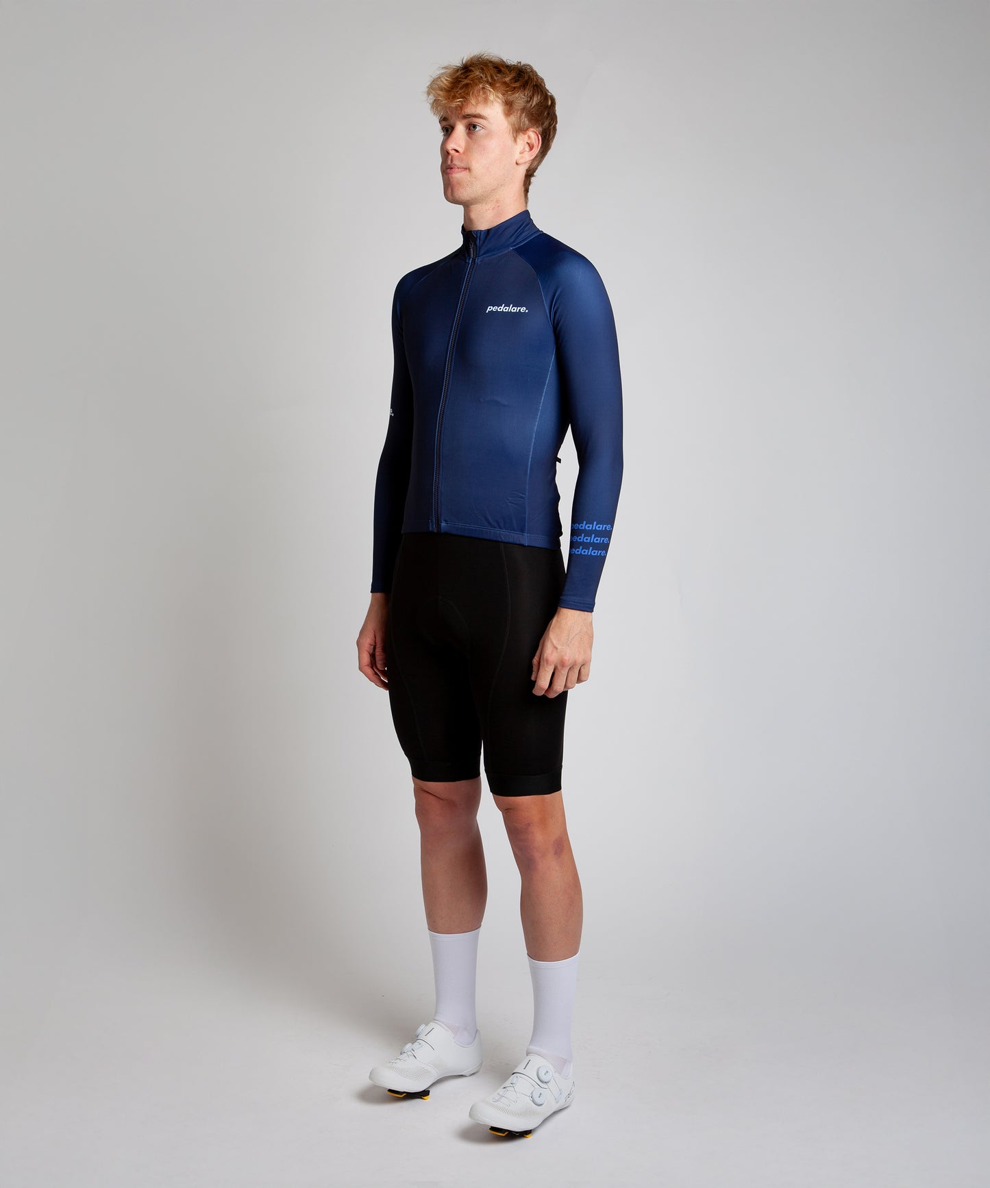 Male cyclist modelling Pedalare’s navy winter long sleeve cycling jersey, paired with black bib shorts. Side profile studio shot highlighting the jersey’s thermal fabric, streamlined fit, and subtle branding. Designed by Perth cycling brand Pedalare for cool-weather performance and style. Men’s winter cycling jersey ideal for road cyclists seeking aero cycling gear and premium cycling apparel.