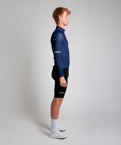 Male cyclist modelling Pedalare’s navy winter long sleeve cycling jersey, paired with black bib shorts. Side profile studio shot highlighting the jersey’s thermal fabric, streamlined fit, and subtle branding. Designed by Perth cycling brand Pedalare for cool-weather performance and style. Men’s winter cycling jersey ideal for road cyclists seeking aero cycling gear and premium cycling apparel.
