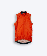 Male cyclist wearing Pedalare’s high-performance orange cycling vest, layered over a navy long sleeve jersey and black bib shorts. Side profile studio shot showcasing the vest’s aerodynamic fit and premium detailing. Lightweight, windproof men’s cycling vest ideal for cool weather rides. Designed by Perth cycling brand Pedalare for performance, comfort, and style. Aero cycling gear for dedicated road cyclists.