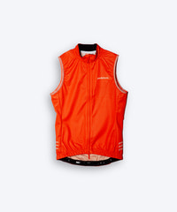 Female cyclist wearing Pedalare’s high-performance orange cycling vest, layered over a navy long sleeve jersey and black bib shorts. Side profile studio shot showcasing the vest’s aerodynamic fit and premium detailing. Lightweight, windproof men’s cycling vest ideal for cool weather rides. Designed by Perth cycling brand Pedalare for performance, comfort, and style. Aero cycling gear for dedicated road cyclists.