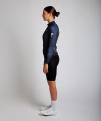 Female cyclist modelling Pedalare’s navy blue winter long sleeve cycling jersey, paired with black bib shorts. Side profile studio shot highlighting the jersey’s thermal fabric, streamlined fit, and subtle branding. Designed by Perth cycling brand Pedalare for cool-weather performance and style. Men’s winter cycling jersey ideal for road cyclists seeking aero cycling gear and premium cycling apparel.