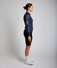 Female cyclist modelling Pedalare’s navy blue winter long sleeve cycling jersey, paired with black bib shorts. Side profile studio shot highlighting the jersey’s thermal fabric, streamlined fit, and subtle branding. Designed by Perth cycling brand Pedalare for cool-weather performance and style. Men’s winter cycling jersey ideal for road cyclists seeking aero cycling gear and premium cycling apparel.