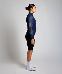 Female cyclist wearing Pedalare’s high-performance navy, blue cycling vest, layered over a navy long sleeve jersey and black bib shorts. Side profile studio shot showcasing the vest’s aerodynamic fit and premium detailing. Lightweight, windproof men’s cycling vest ideal for cool weather rides. Designed by Perth cycling brand Pedalare for performance, comfort, and style. Aero cycling gear for dedicated road cyclists.