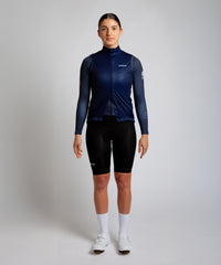 Female cyclist wearing Pedalare’s high-performance navy, blue cycling vest, layered over a navy long sleeve jersey and black bib shorts. Side profile studio shot showcasing the vest’s aerodynamic fit and premium detailing. Lightweight, windproof men’s cycling vest ideal for cool weather rides. Designed by Perth cycling brand Pedalare for performance, comfort, and style. Aero cycling gear for dedicated road cyclists.