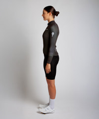 Female cyclist modelling Pedalare’s green winter long sleeve cycling jersey, paired with black bib shorts. Side profile studio shot highlighting the jersey’s thermal fabric, streamlined fit, and subtle branding. Designed by Perth cycling brand Pedalare for cool-weather performance and style. Men’s winter cycling jersey ideal for road cyclists seeking aero cycling gear and premium cycling apparel.