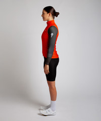 Female cyclist wearing Pedalare’s high-performance orange cycling vest, layered over a navy long sleeve jersey and black bib shorts. Side profile studio shot showcasing the vest’s aerodynamic fit and premium detailing. Lightweight, windproof men’s cycling vest ideal for cool weather rides. Designed by Perth cycling brand Pedalare for performance, comfort, and style. Aero cycling gear for dedicated road cyclists.