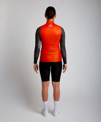 Female cyclist wearing Pedalare’s high-performance orange cycling vest, layered over a navy long sleeve jersey and black bib shorts. Side profile studio shot showcasing the vest’s aerodynamic fit and premium detailing. Lightweight, windproof men’s cycling vest ideal for cool weather rides. Designed by Perth cycling brand Pedalare for performance, comfort, and style. Aero cycling gear for dedicated road cyclists.
