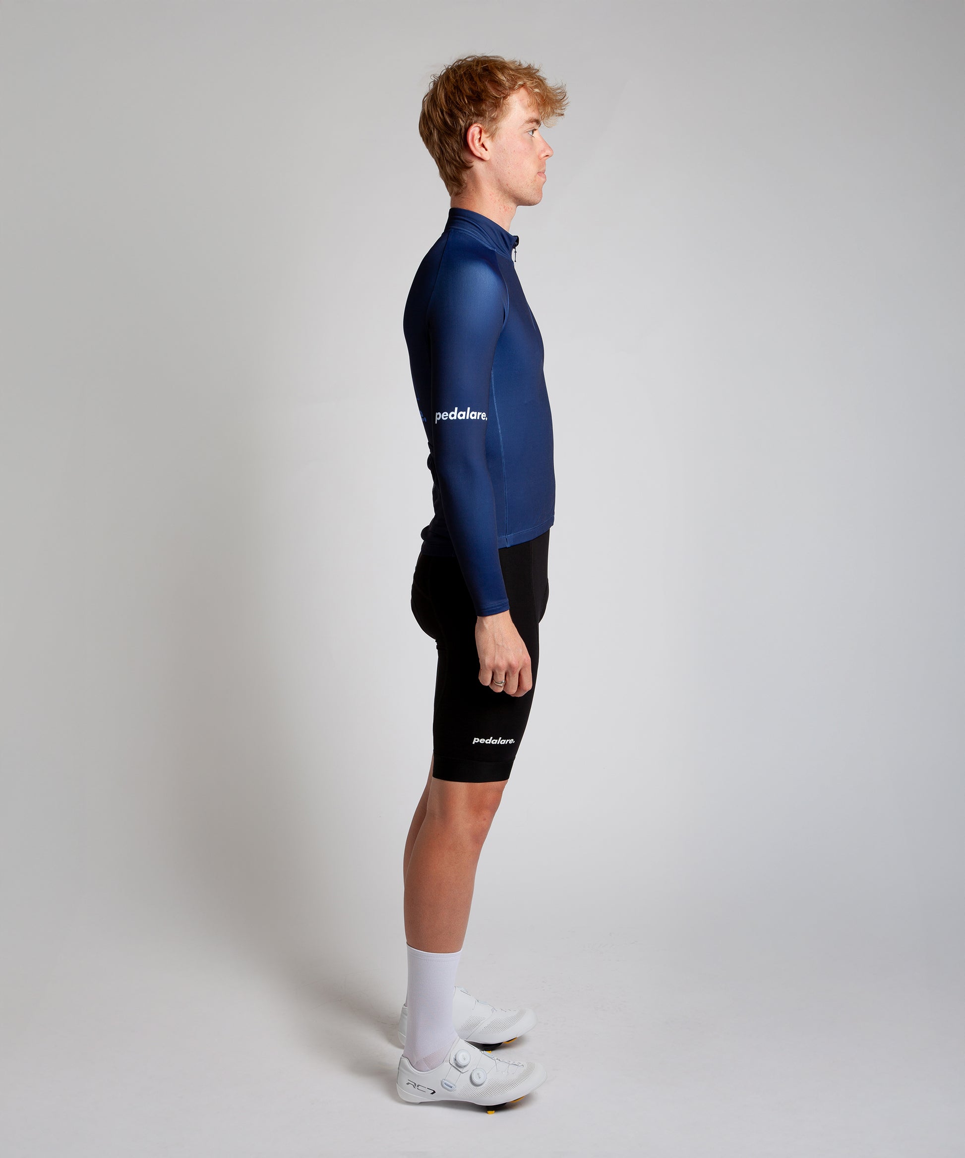 Male cyclist modelling Pedalare’s navy winter long sleeve cycling jersey, paired with black bib shorts. Side profile studio shot highlighting the jersey’s thermal fabric, streamlined fit, and subtle branding. Designed by Perth cycling brand Pedalare for cool-weather performance and style. Men’s winter cycling jersey ideal for road cyclists seeking aero cycling gear and premium cycling apparel.