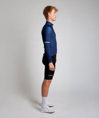 Male cyclist modelling Pedalare’s navy winter long sleeve cycling jersey, paired with black bib shorts. Side profile studio shot highlighting the jersey’s thermal fabric, streamlined fit, and subtle branding. Designed by Perth cycling brand Pedalare for cool-weather performance and style. Men’s winter cycling jersey ideal for road cyclists seeking aero cycling gear and premium cycling apparel.