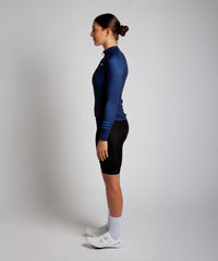 Female cyclist modelling Pedalare’s navy blue winter long sleeve cycling jersey, paired with black bib shorts. Side profile studio shot highlighting the jersey’s thermal fabric, streamlined fit, and subtle branding. Designed by Perth cycling brand Pedalare for cool-weather performance and style. Men’s winter cycling jersey ideal for road cyclists seeking aero cycling gear and premium cycling apparel.